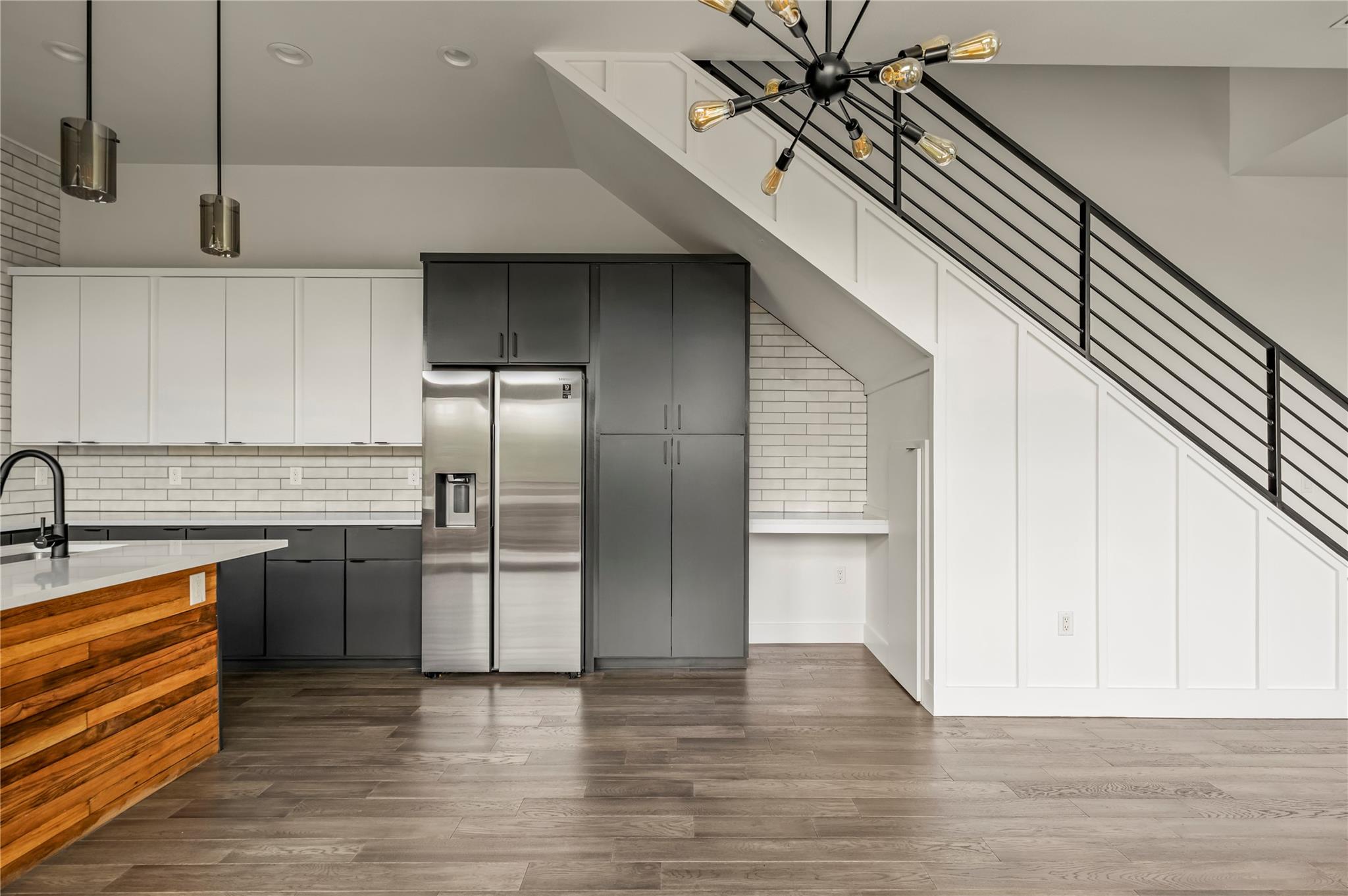 Modern kitchen with charcoal cabinetry, stainless steel refrigerator, wood-front island, and staircase overhead.
