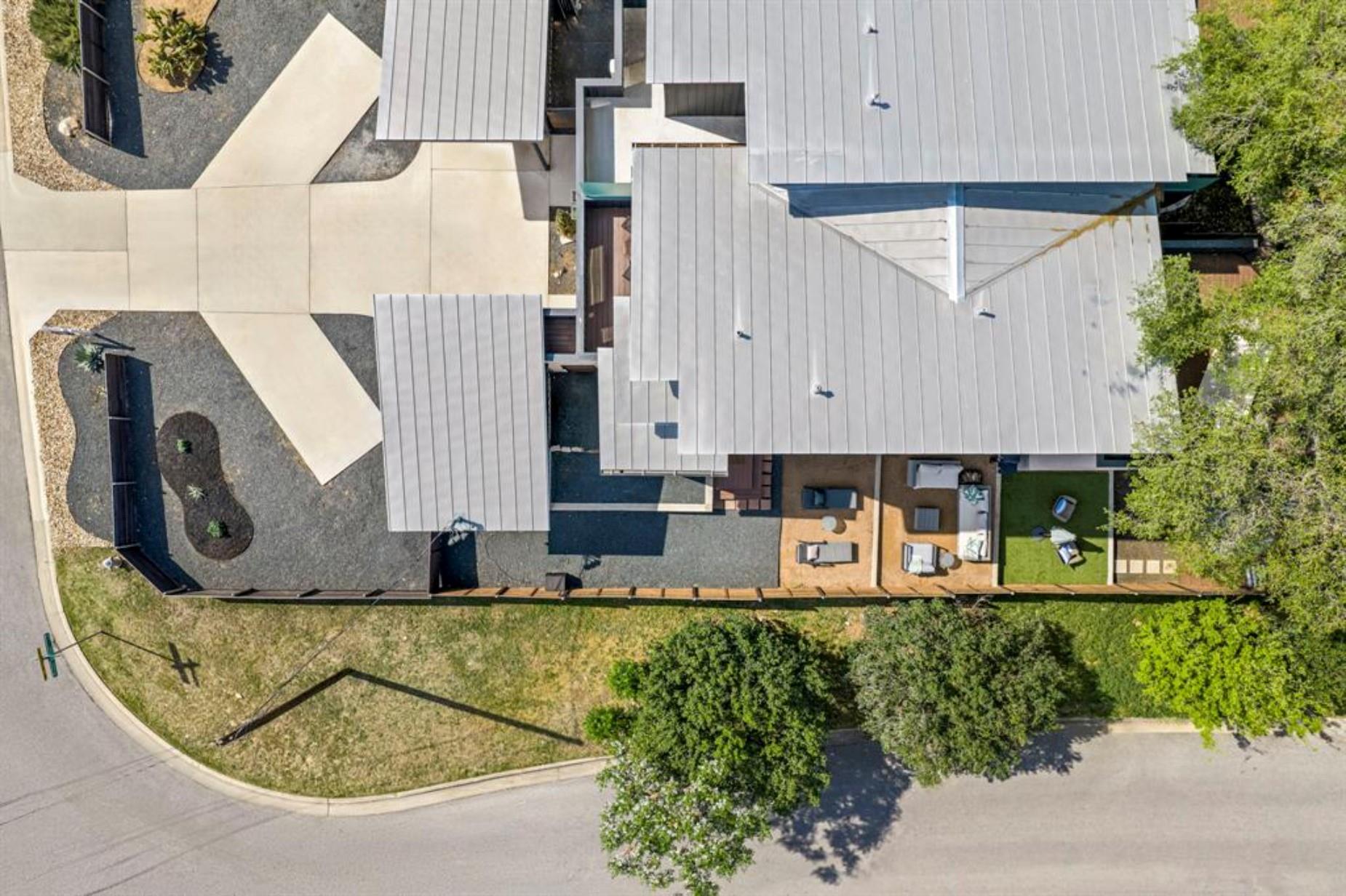 Aerial view of a modern home with gray metal roofs, gravel landscaping, and a fenced patio and lawn.