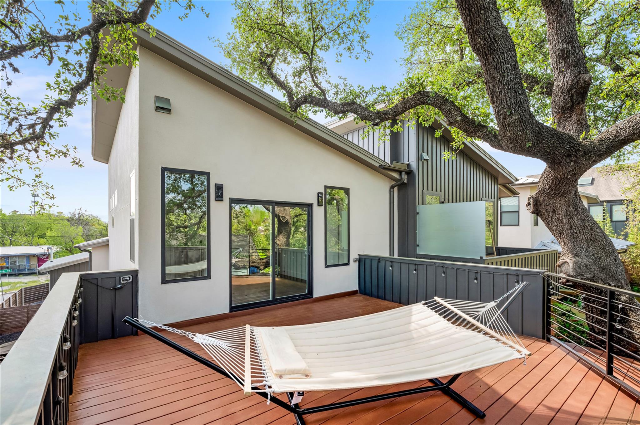Raised deck with a white hammock beside a modern home, shaded by a large oak tree.
