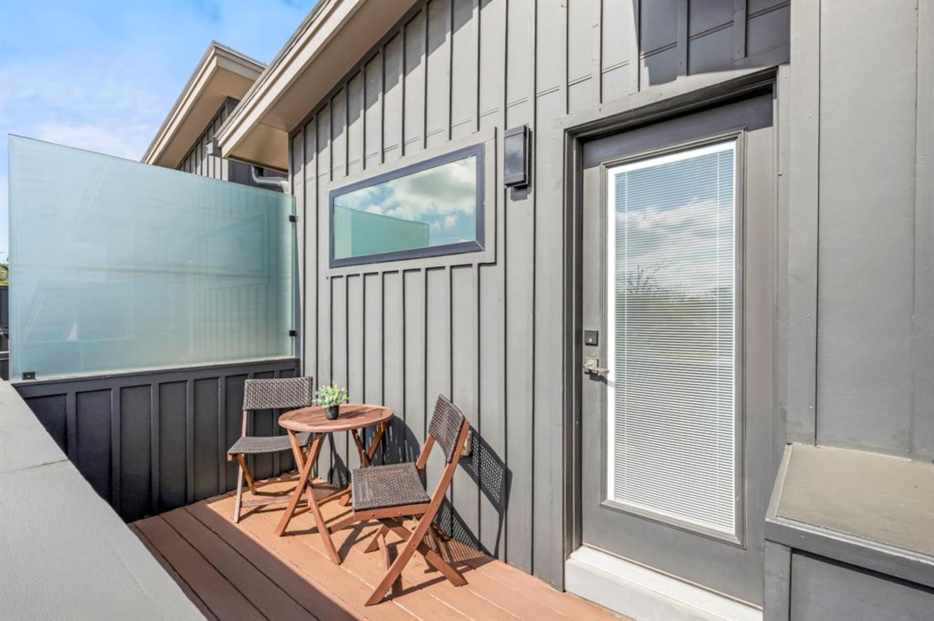 Private deck with a small table and chairs beside gray siding and a glass privacy screen.