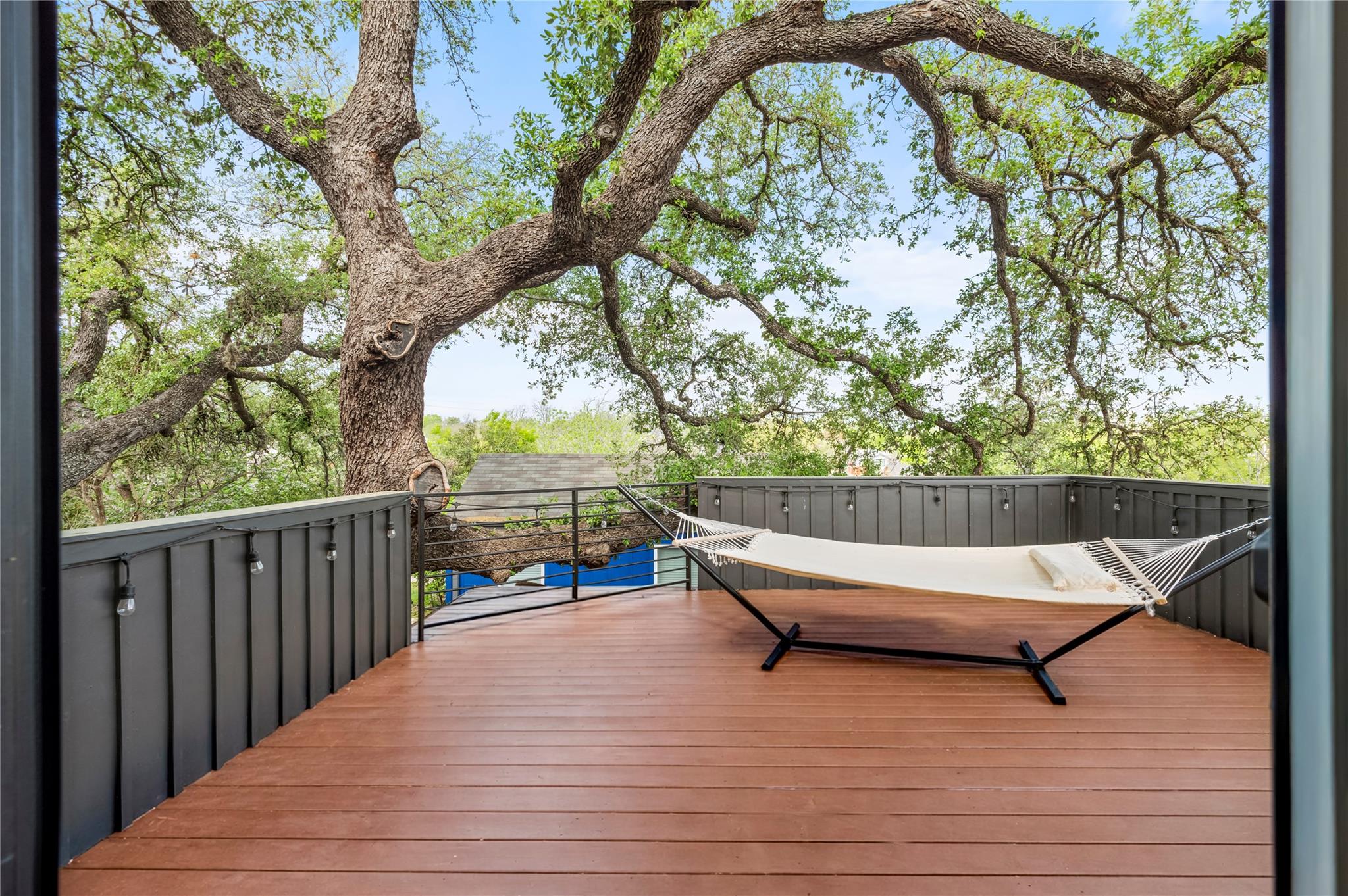 Elevated wood deck beneath a sprawling oak tree, furnished with a cream hammock.