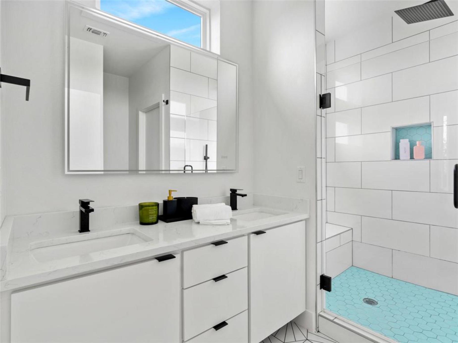 Modern bathroom with a white double vanity and glass shower featuring turquoise hexagonal tile.