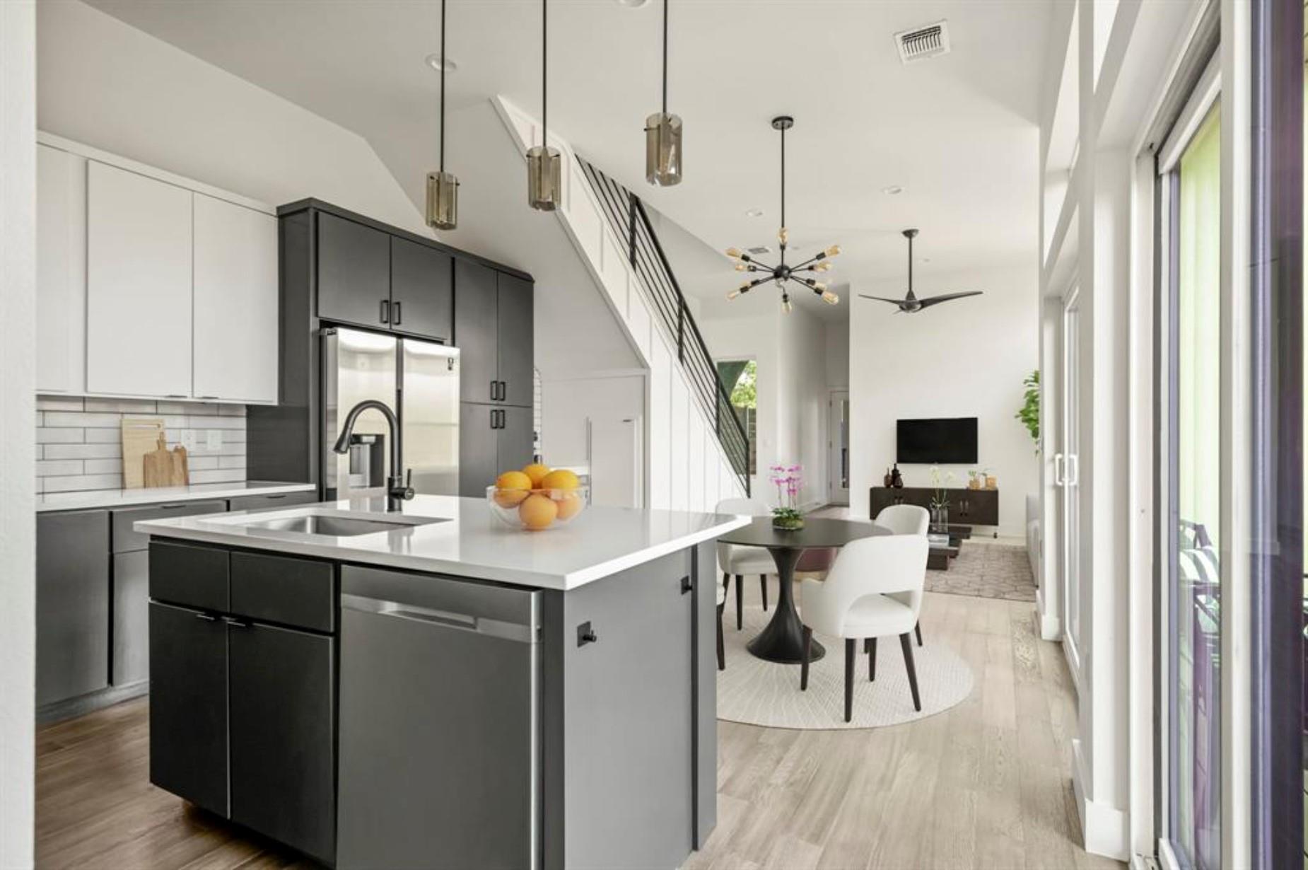 Open-plan kitchen with dark cabinets, a large white island, and a dining area beside tall windows.