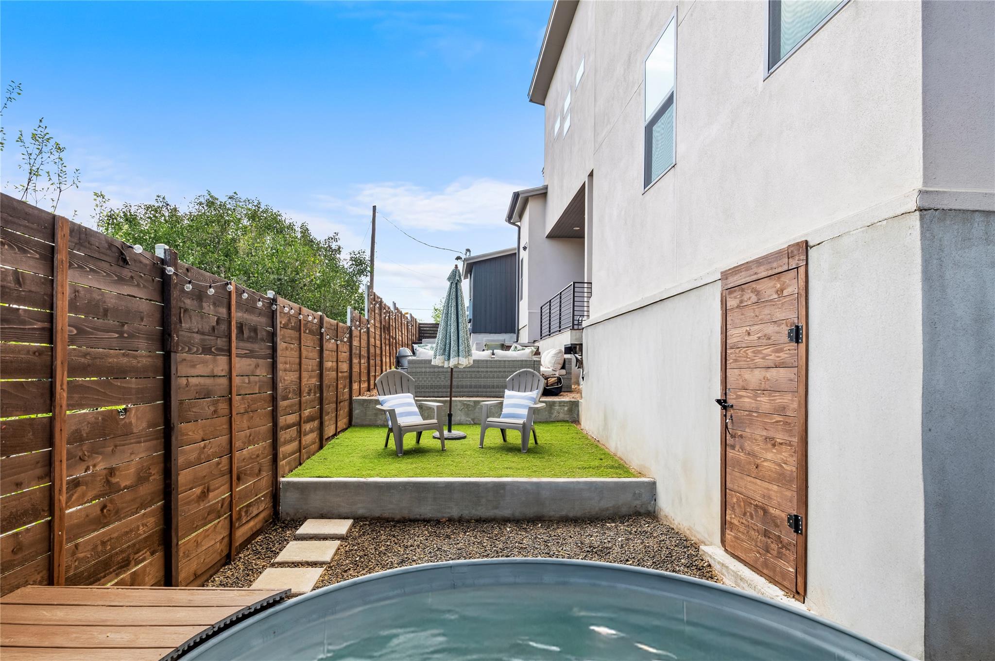 Fenced backyard with a curved pool and raised turf seating area beside the home.