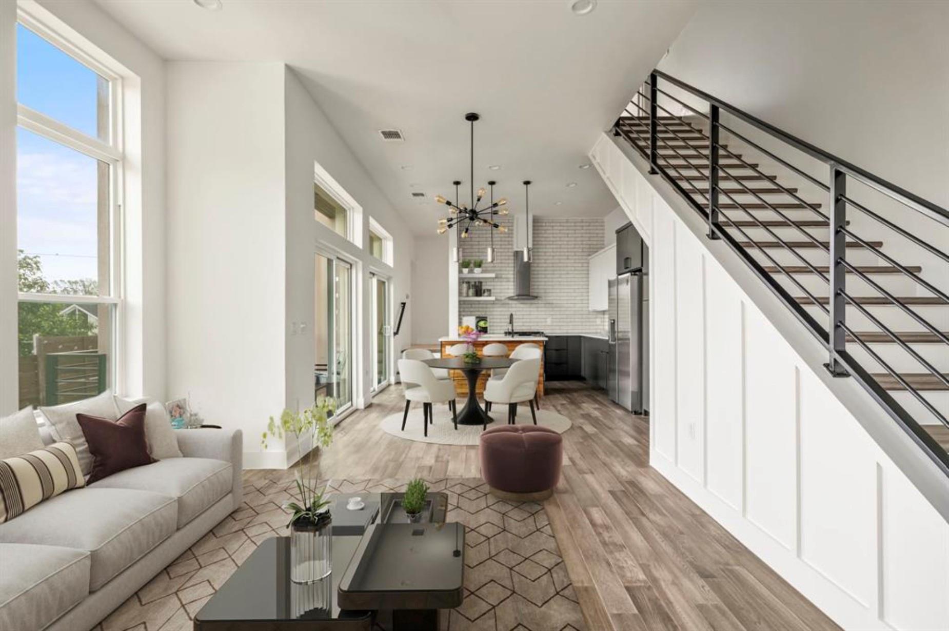 Open-plan living room and kitchen with tall windows and a modern black-railed staircase.