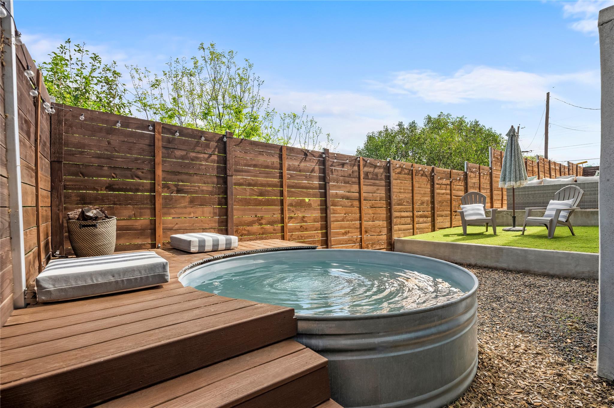 Backyard pool beside a raised wooden deck, with a fenced seating area and string lights.