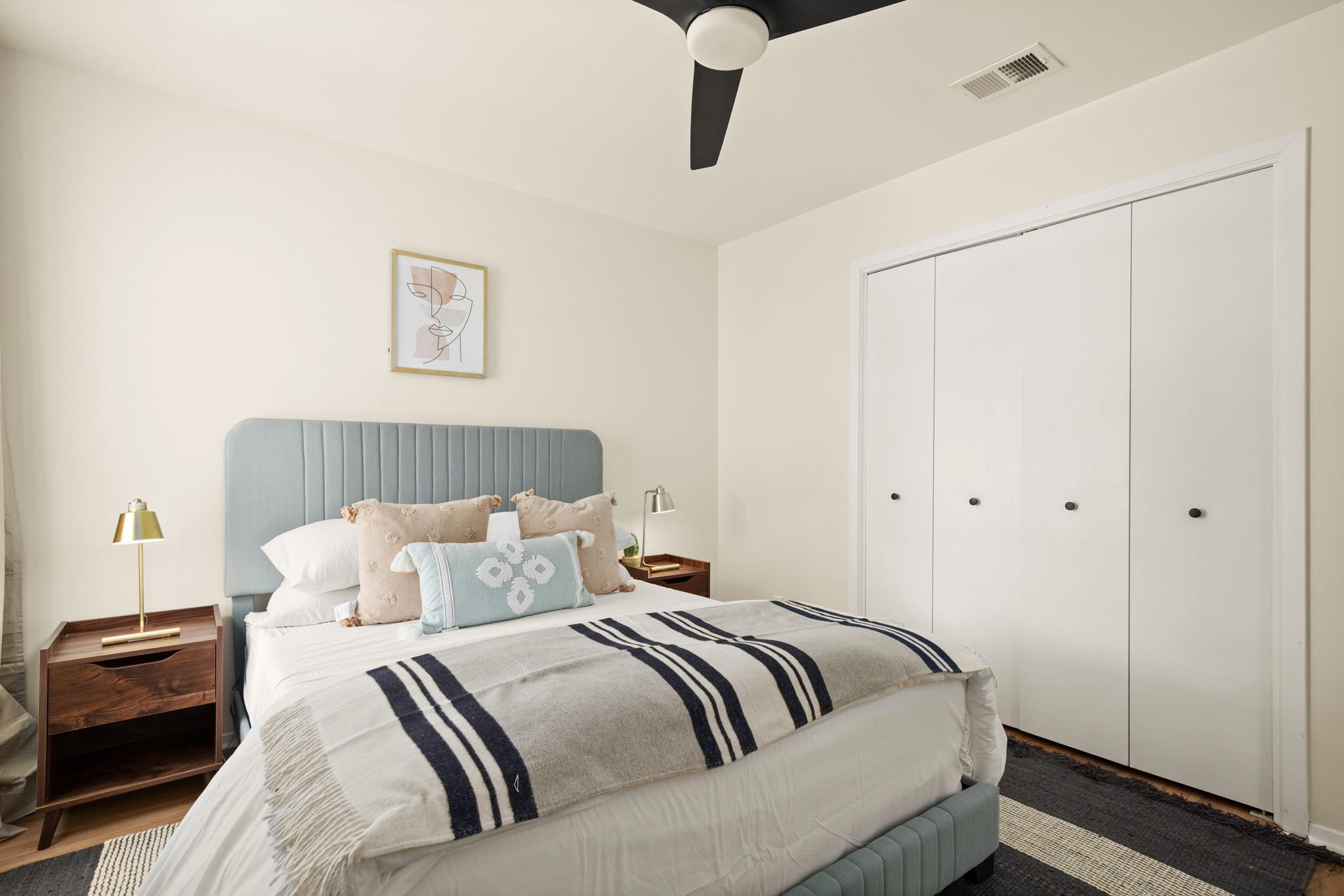 Bedroom with a blue upholstered headboard, striped blanket, and wall-length white closet.