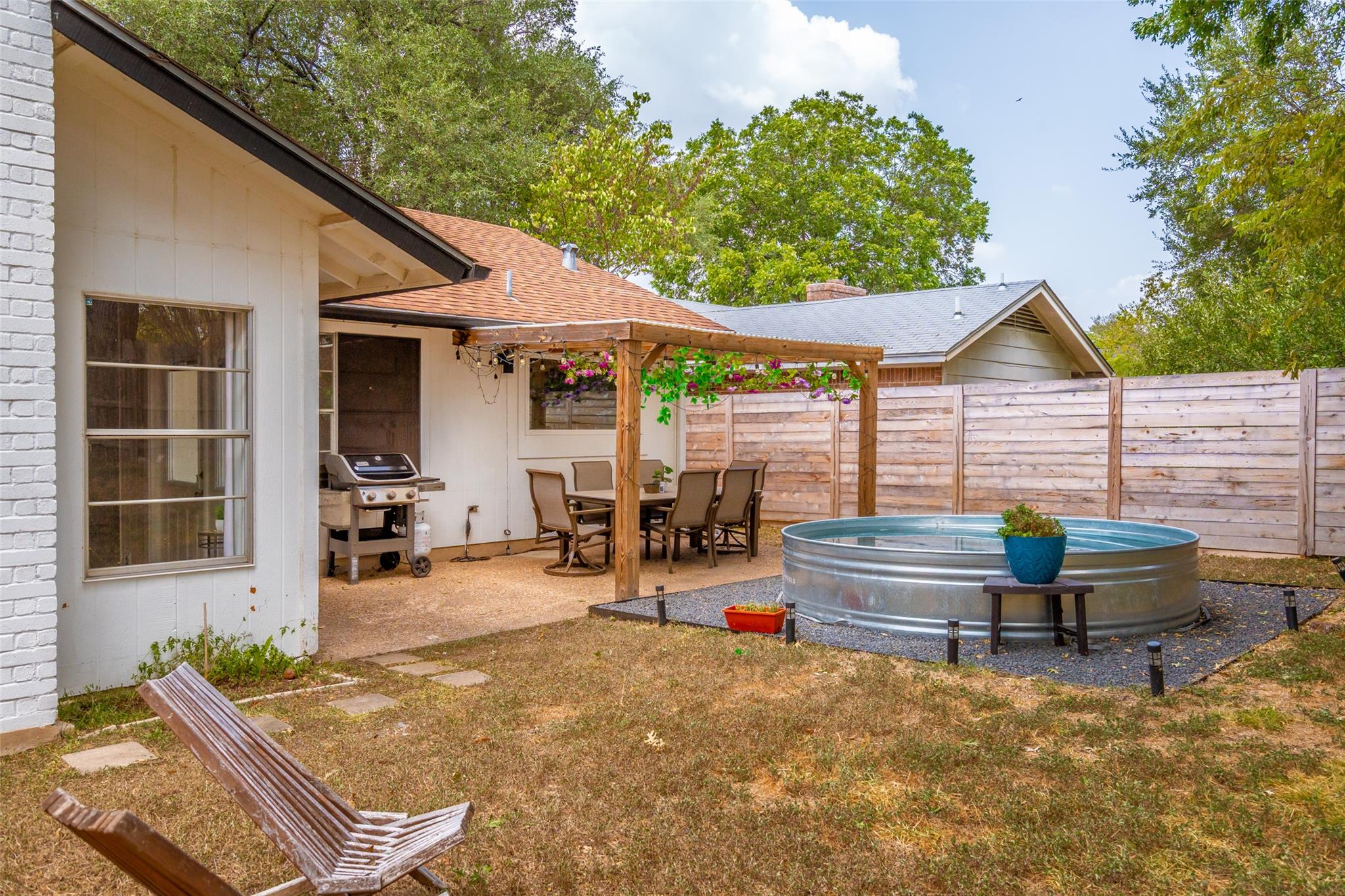Backyard patio with a round stock-tank pool beside a pergola-covered dining area.