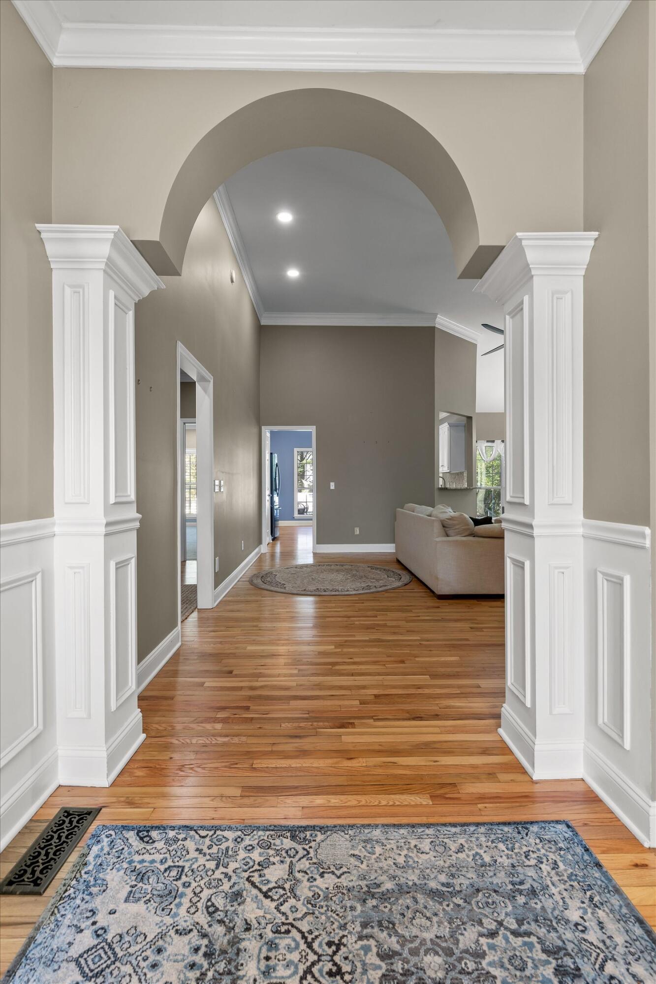 Foyer with a large arch, white paneled columns, hardwood floors, and a patterned rug.