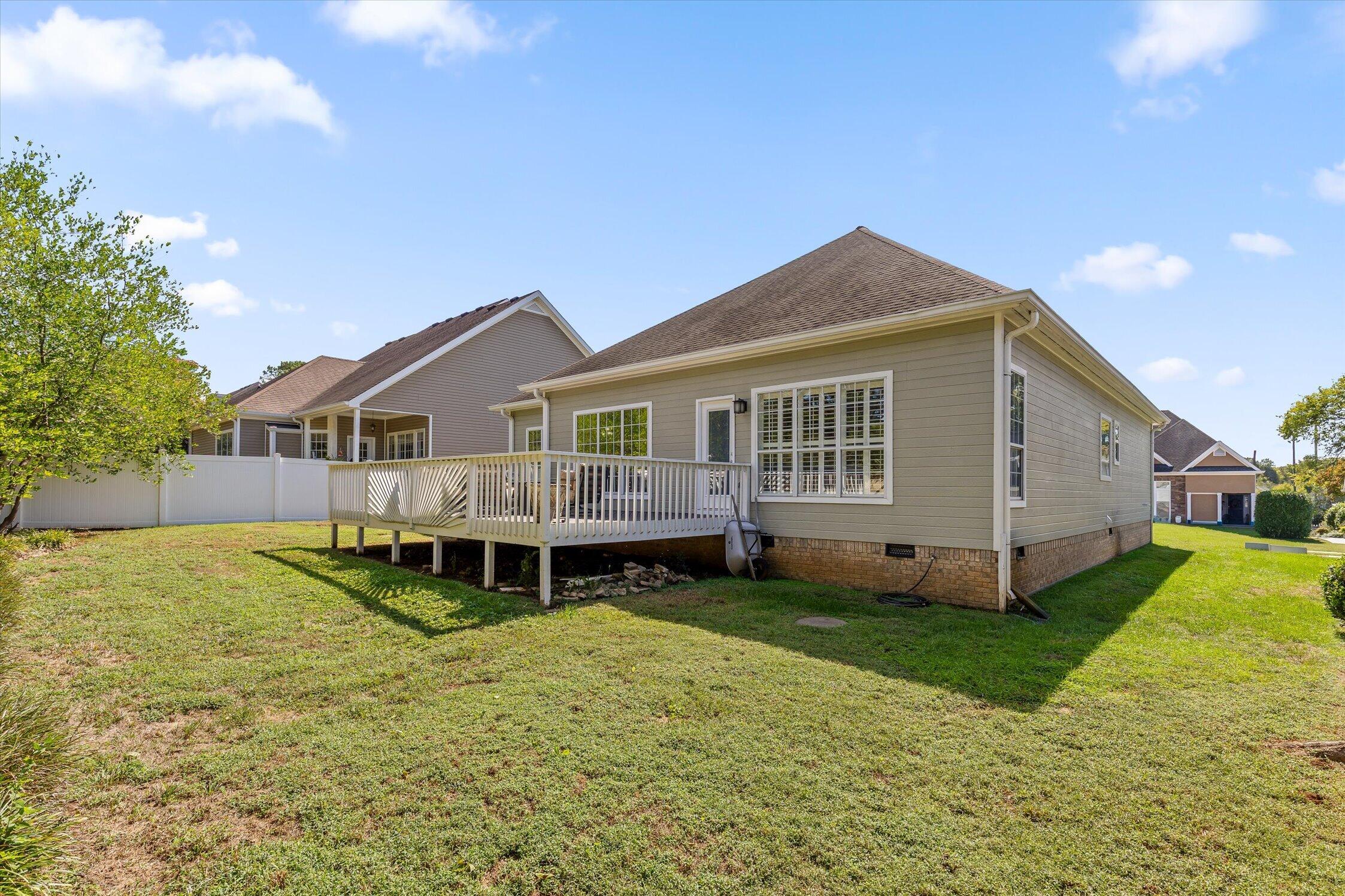 Rear of a beige home with a raised white deck and broad lawn.