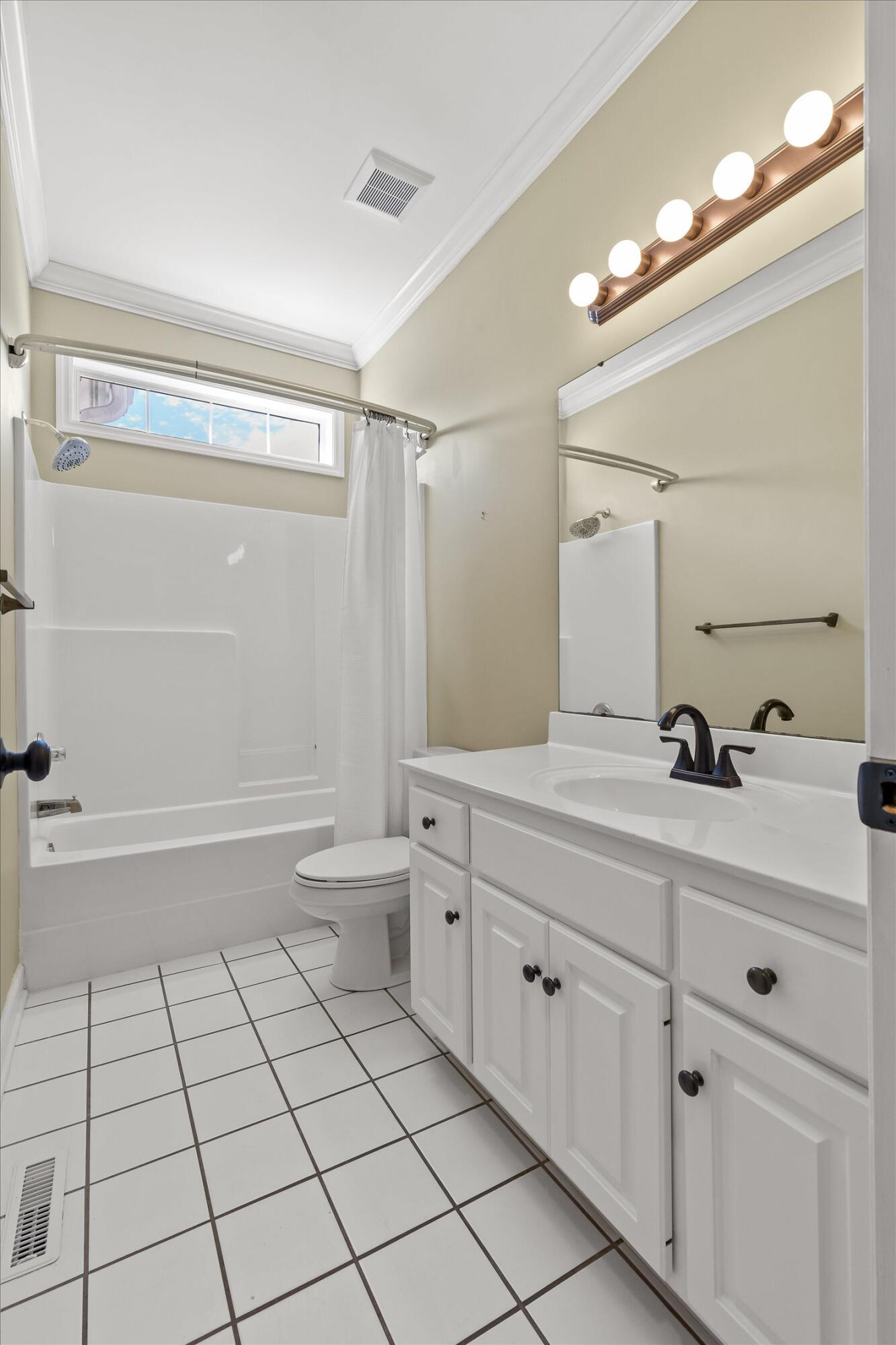 Bathroom with a white tub-shower, tiled floor, and white vanity beneath a large mirror.