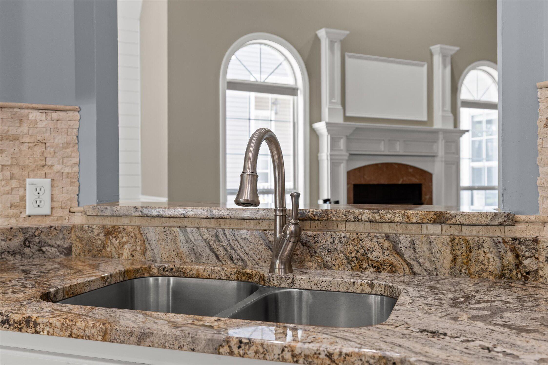Double-basin sink and tall faucet in a speckled granite kitchen counter, with a fireplace beyond.