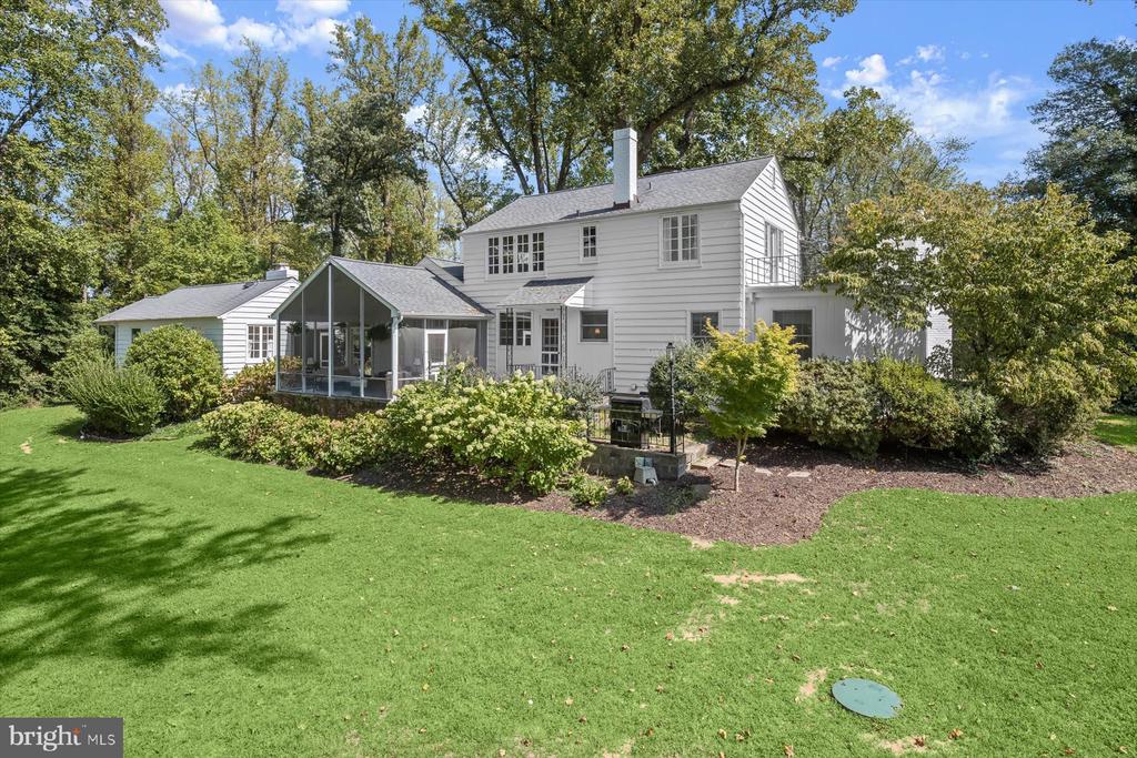 White two-story house with a glass-enclosed sunroom and landscaped backyard.
