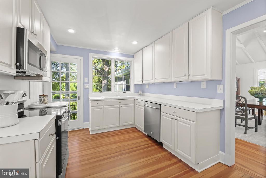 Bright kitchen with white cabinetry, lavender walls, stainless appliances, and warm wood floors.