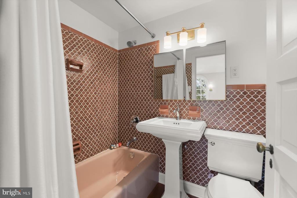 Bathroom with patterned terracotta tile, a peach bathtub, and a white pedestal sink.