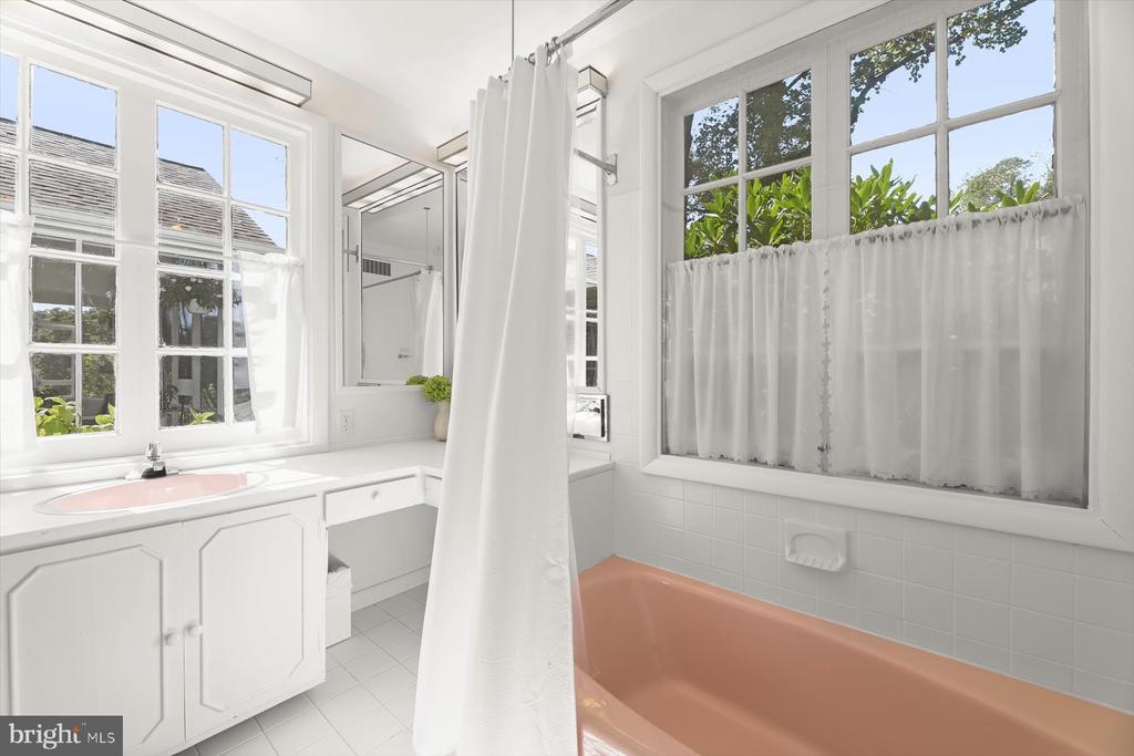 Bathroom with a peach-colored bathtub, white shower curtain, and large windows.