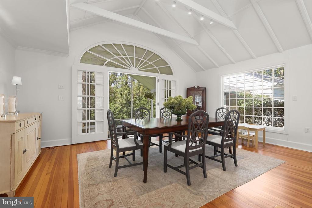 Dining room with vaulted beam ceiling, arched glass doors, and a dark wood table on a rug.