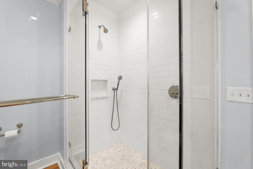 Walk-in shower with white subway tile, glass enclosure, handheld showerhead, and mosaic floor.
