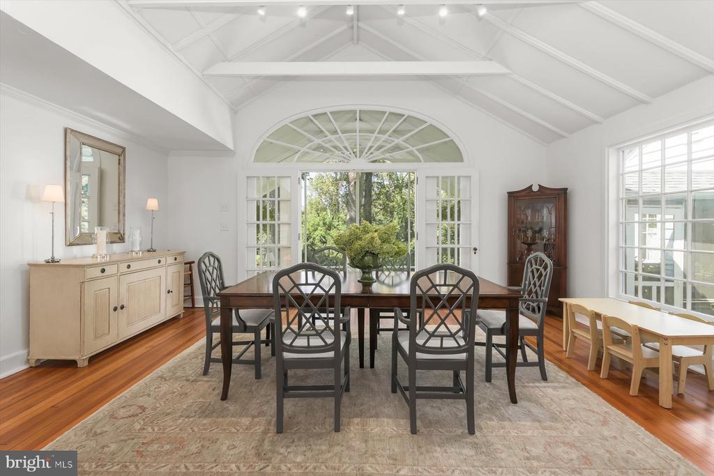 Dining room with a long dark wood table beneath a vaulted ceiling and arched window.