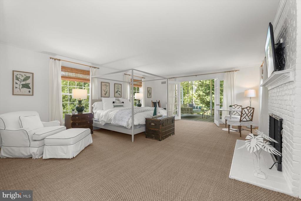 Furnished bedroom with a canopy bed, white brick fireplace, and French doors opening to greenery.