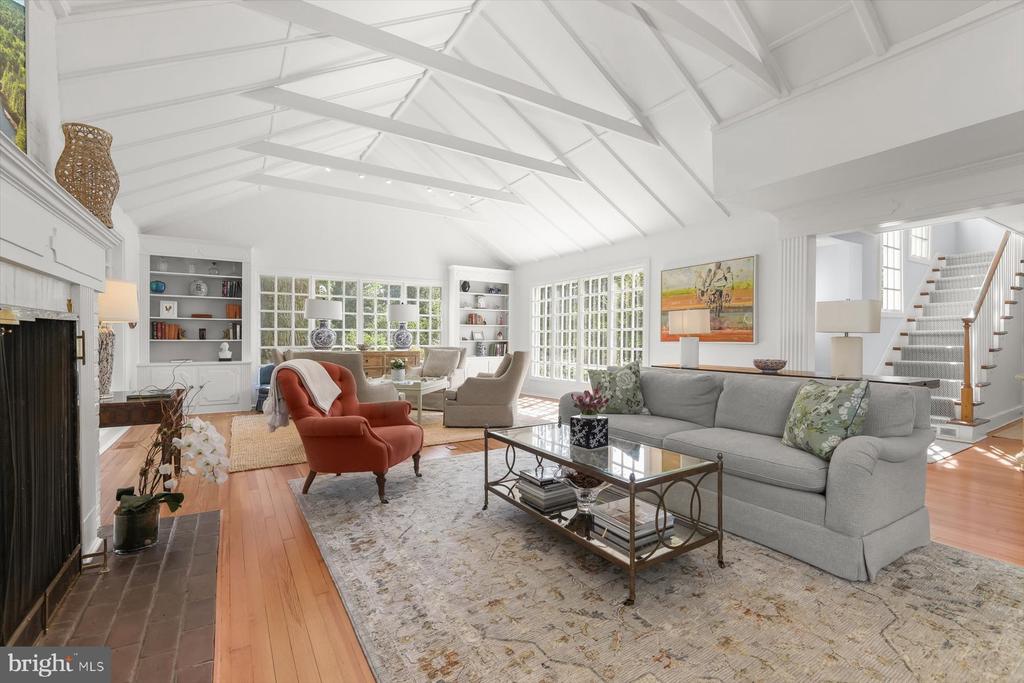 Living room with vaulted beamed ceiling, gray sofa, fireplace, and staircase.