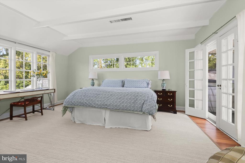 Spacious bedroom with a king bed, tray ceiling, broad windows, and French doors opening to a deck.