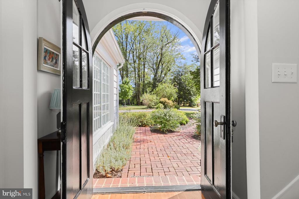 Arched entryway with open black doors framing a brick path and leafy garden.
