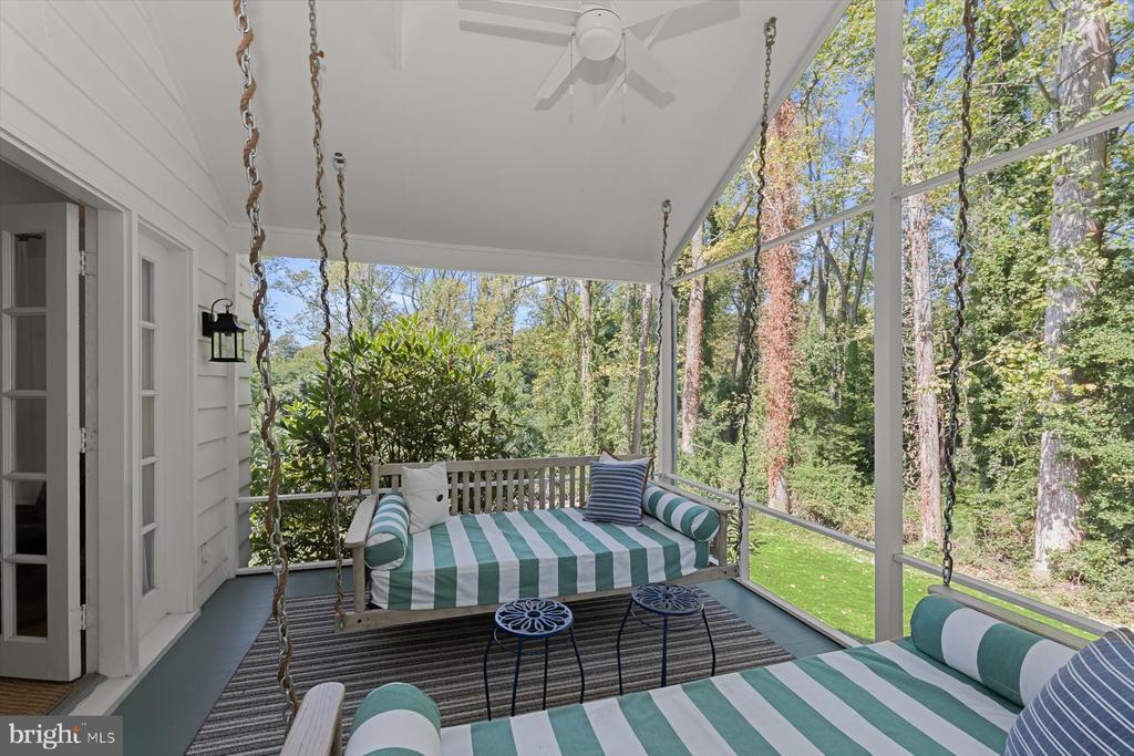 Screened porch with striped swing seating and a wooded view.