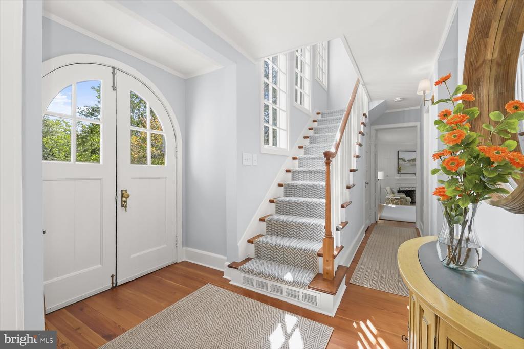 Entry foyer with an arched front door, hardwood floors, and a carpeted staircase with a wood handrail.