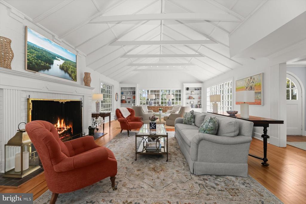 Living room with vaulted beam ceiling, fireplace, large windows, and gray and rust-colored seating.