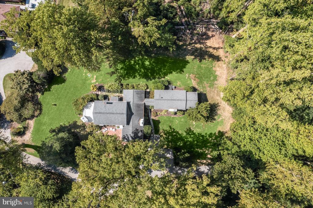 Aerial view of a gray-roofed home surrounded by lawn and mature trees.