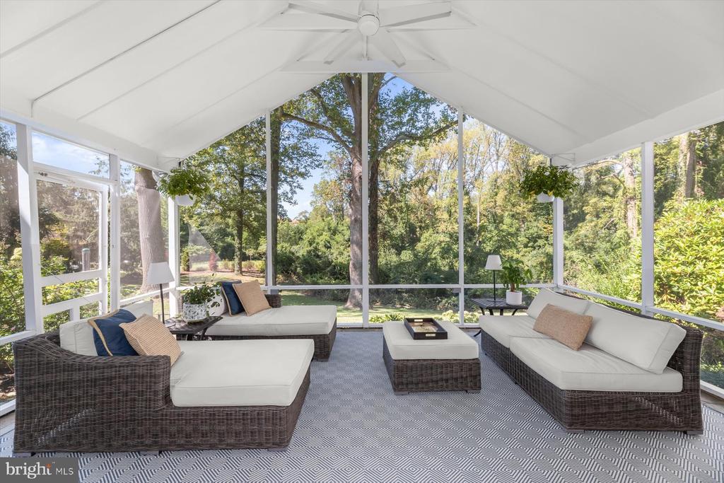 Furnished screened sunroom with vaulted ceiling, wicker lounge seating, and leafy garden views.