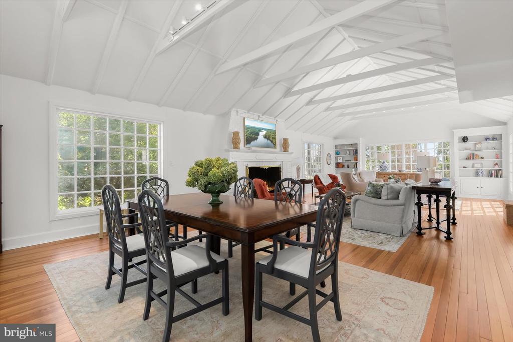 Dining room and living area with vaulted beams, hardwood floors, and large windows.