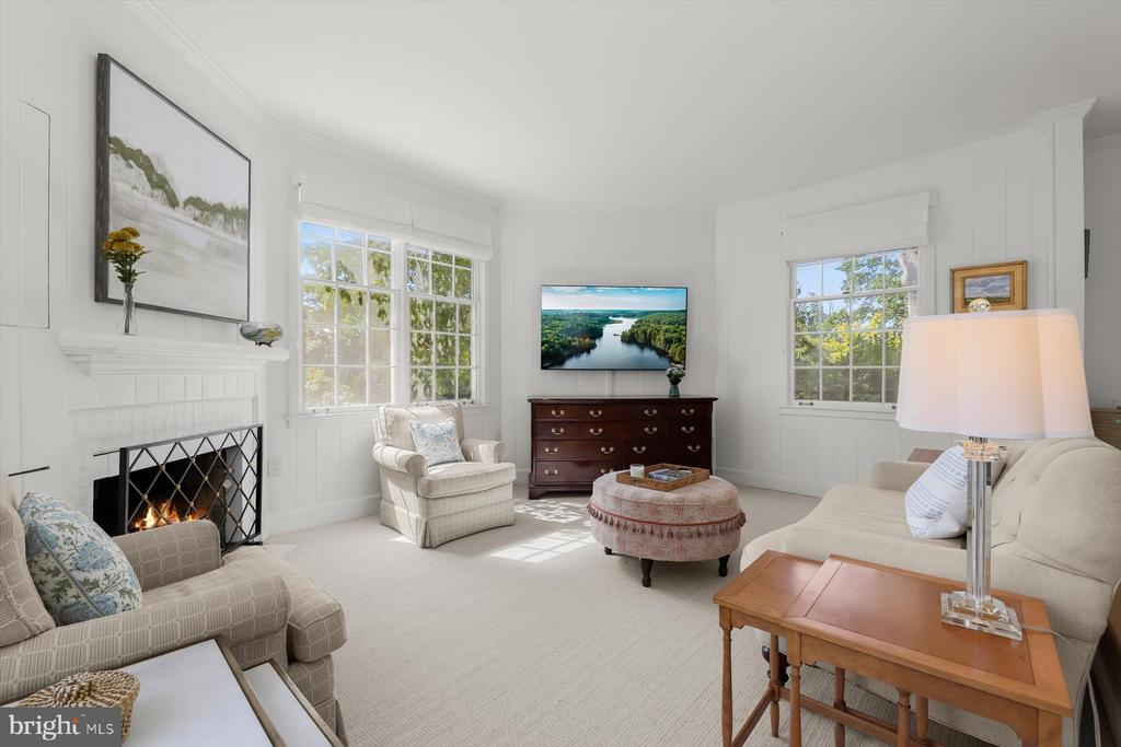 Living room with a white-paneled fireplace, large windows, and cream seating.