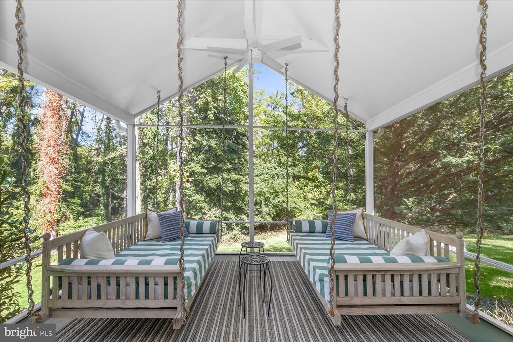 Screened porch with striped daybeds, a ceiling fan, and leafy wooded views.
