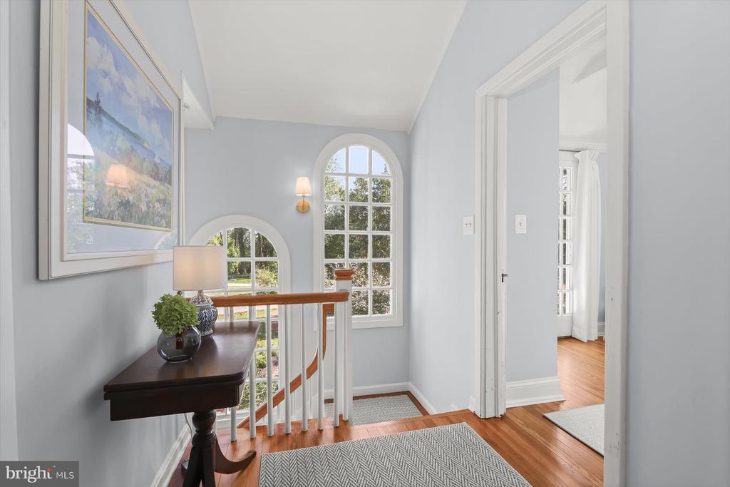 Upstairs landing with tall arched windows, a dark console table, and polished wood floors.