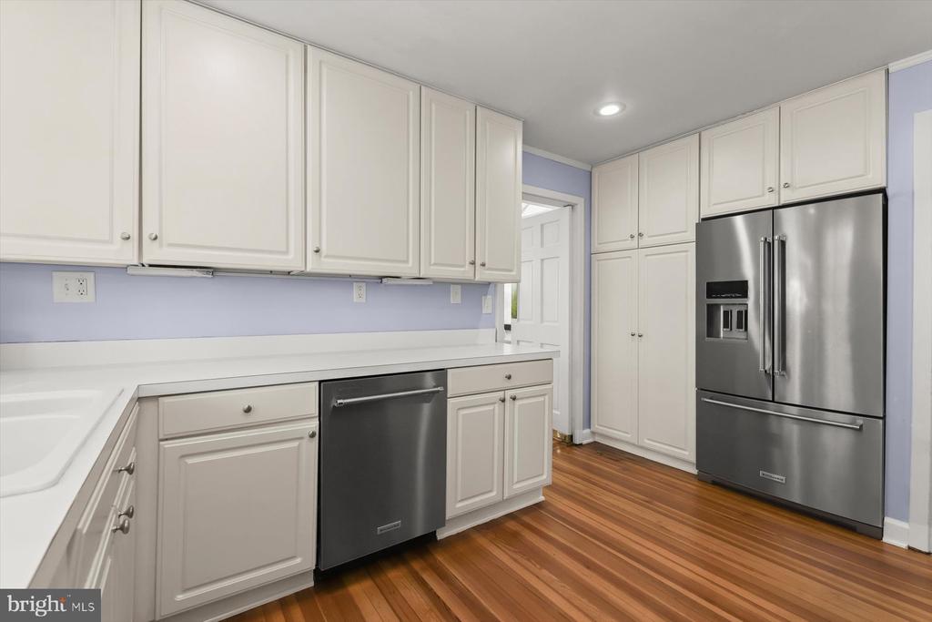 Kitchen with white cabinets, stainless steel appliances, lavender walls, and hardwood flooring.