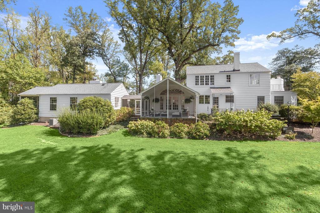 White two-story home with a covered gabled porch, landscaped yard, and mature trees.