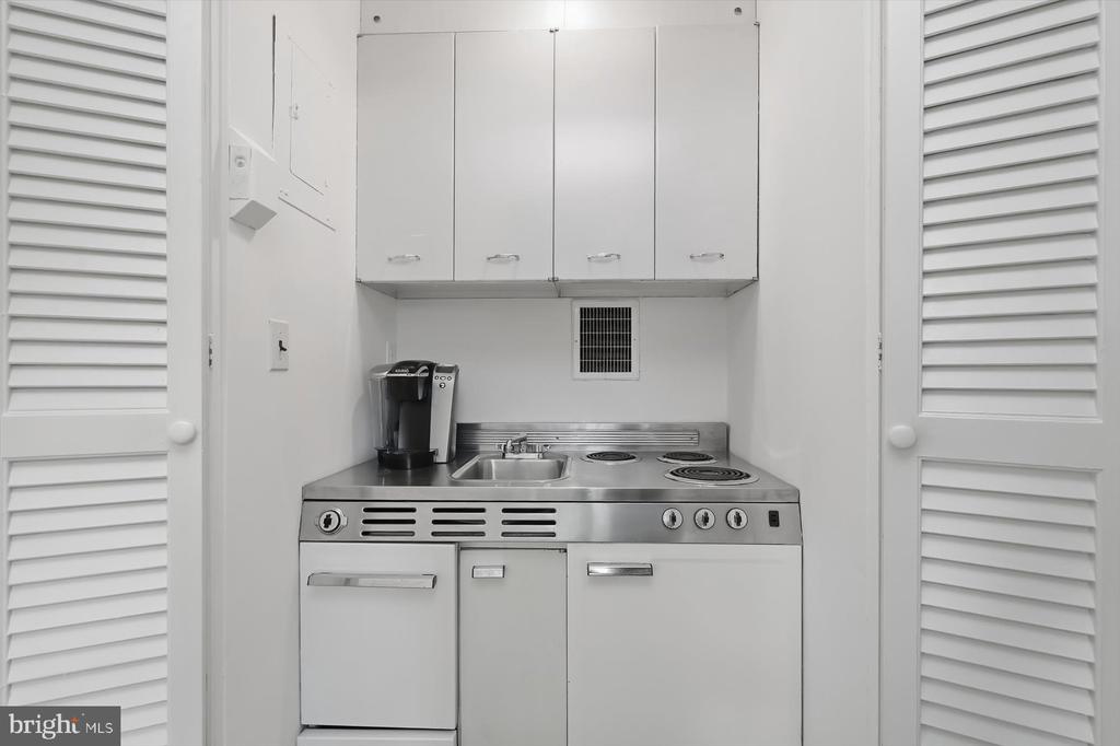 Compact kitchenette with white cabinets, stainless-steel counter, sink, and electric cooktop.
