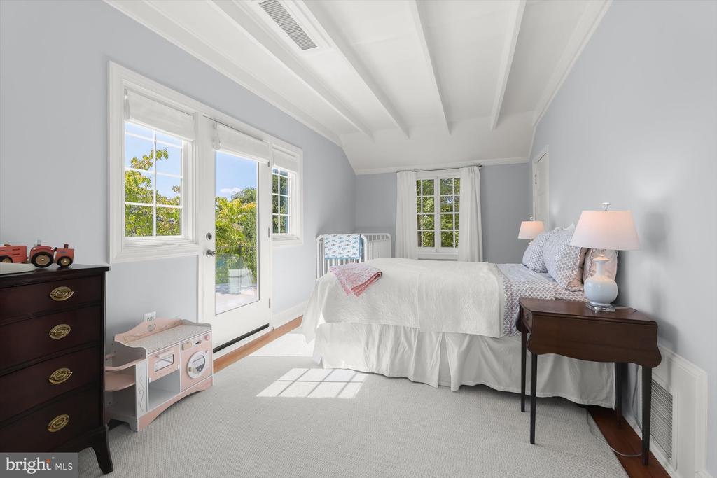 Bedroom with white bed, exposed ceiling beams, and a glass door opening toward greenery.