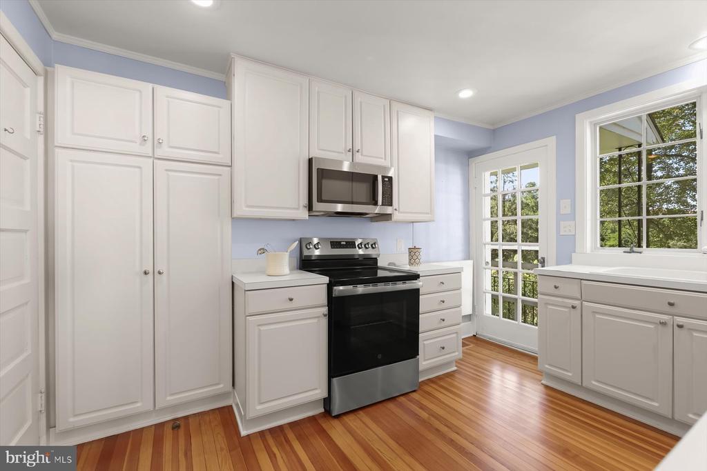 Kitchen with white cabinets, black appliances, striped hardwood floors, and a glass-paned door.