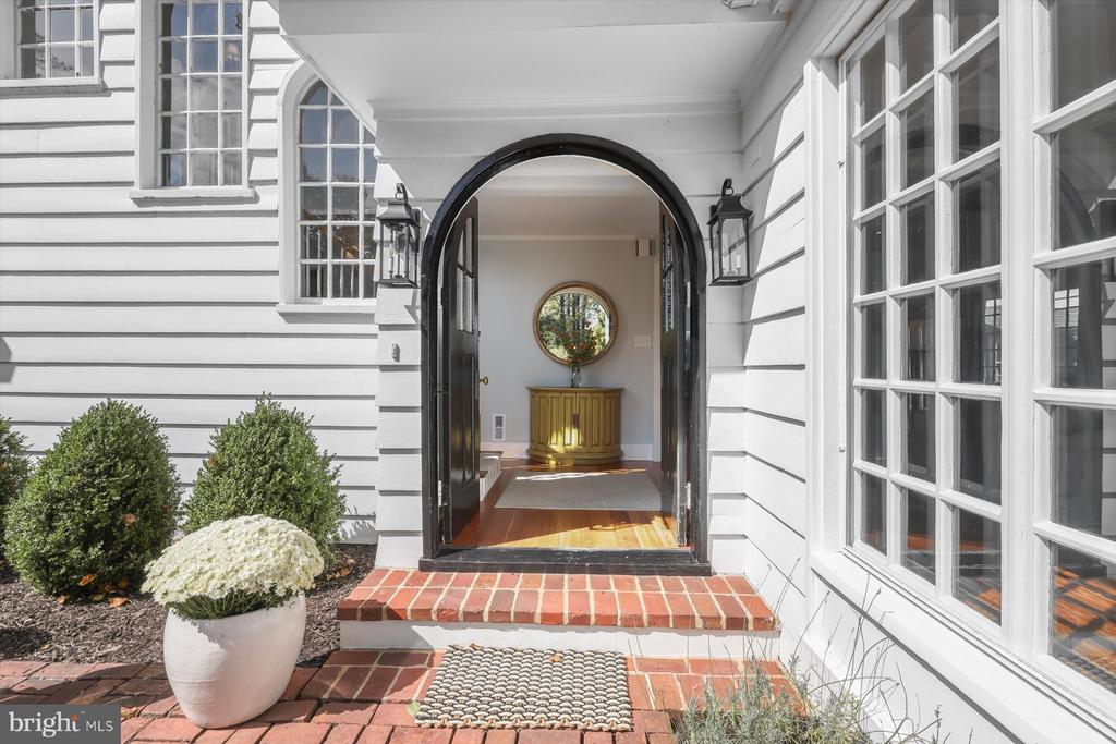 White house entrance with a black arched doorway, brick steps, and a round foyer window.