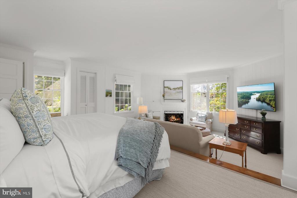 Bedroom with a white bed opening into a sitting area with a fireplace and bright windows.