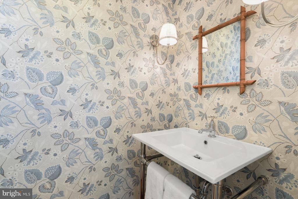 Bathroom sink with exposed chrome plumbing, botanical wallpaper, and a wooden-framed mirror.