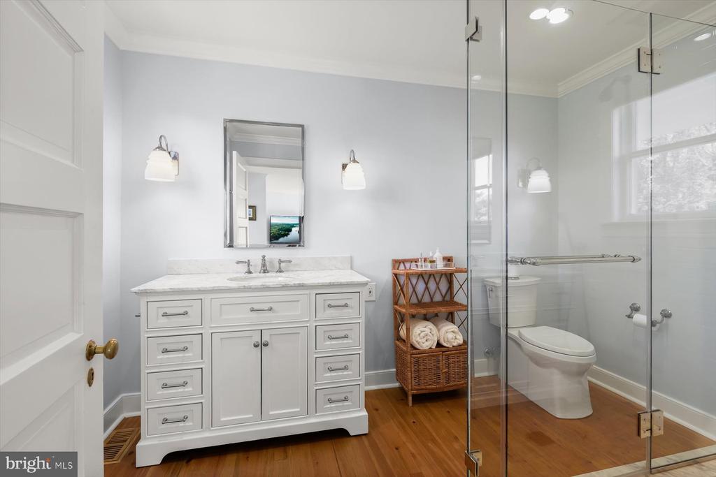Bathroom with a white vanity, glass shower enclosure, and warm wood flooring.