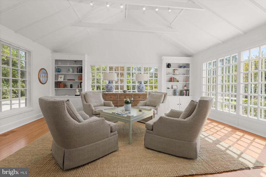 Living room with vaulted ceiling, built-in bookcases, and large windows surrounding an armchair seating area.
