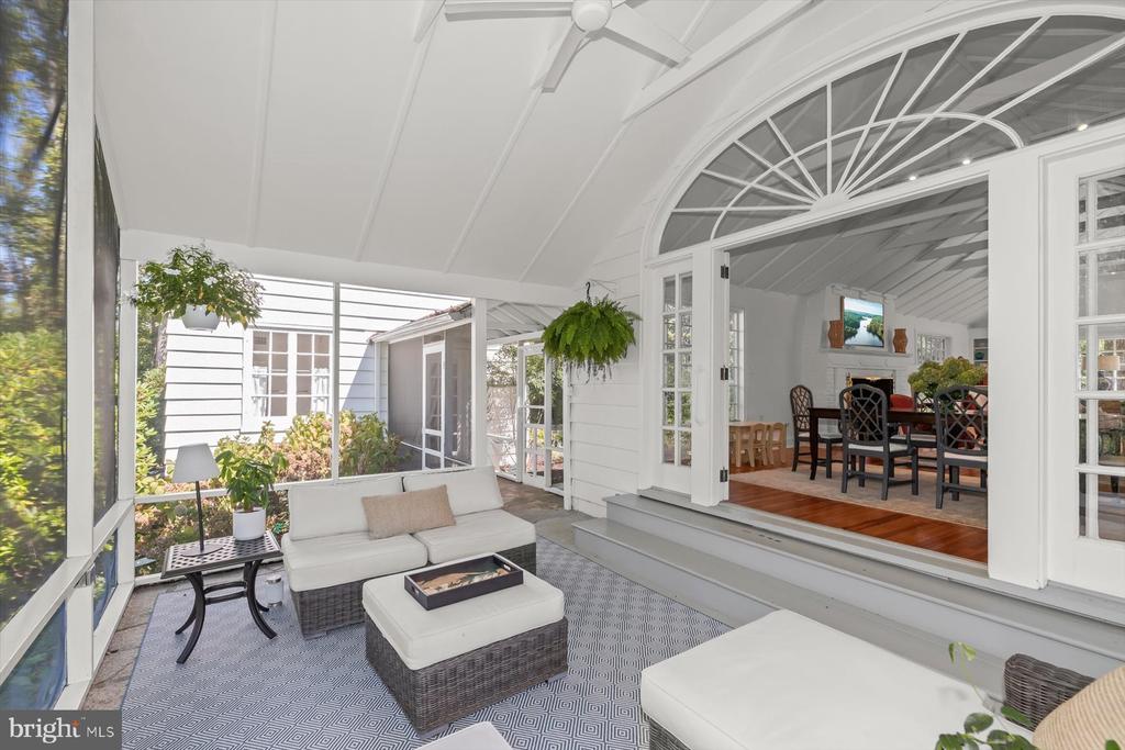 Screened sunroom with white wicker seating and an arched doorway to the dining room.