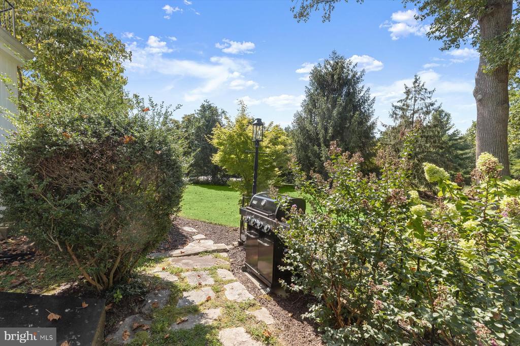 Landscaped backyard with a stone path, stainless-steel grill, lawn, and mature trees.
