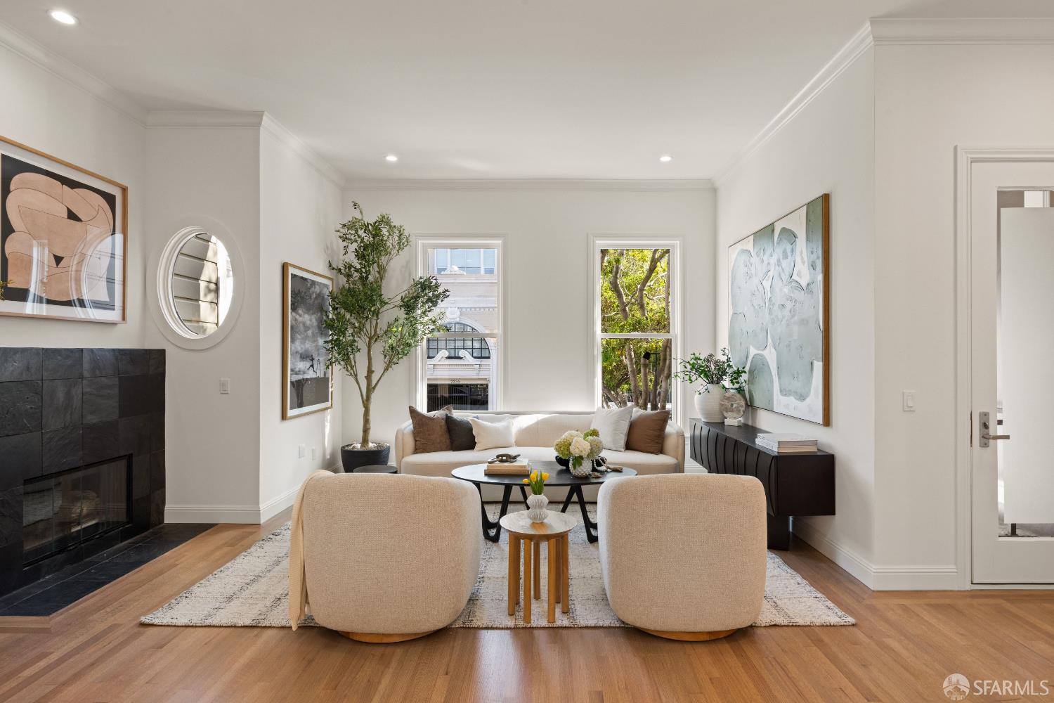Staged living room with cream seating, a black tiled fireplace, hardwood floors, and large windows.