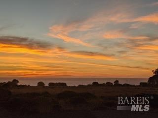 Coastal sunset over the ocean, with orange clouds above dark silhouetted hills.